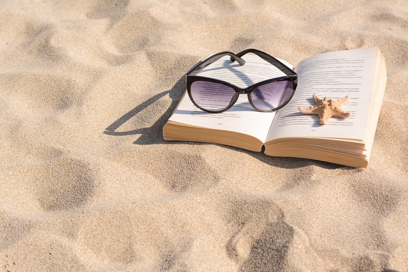 Ein Buch, Sonnenbrillen und ein Seestern im Sand